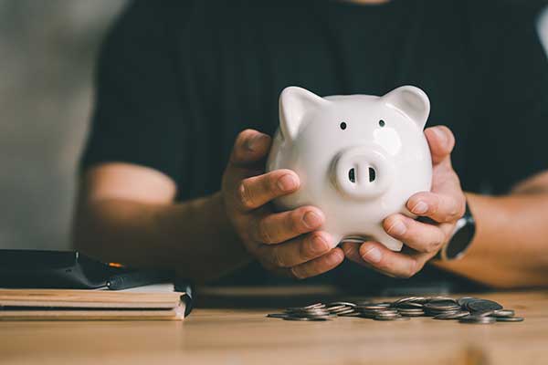 A person holding a piggy bank with coins below it, representing saving money.