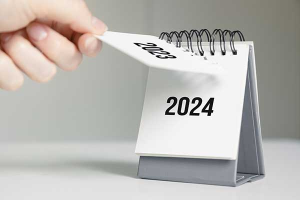 A person tearing off a 2023 calendar to reveal the 2024 calendar underneath.