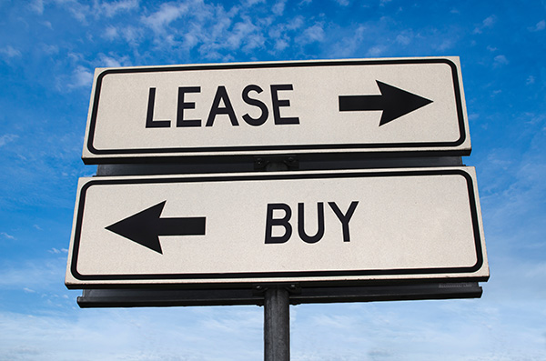 Two street signs pointing in opposite directions. One says "Lease" and the other says "Buy."