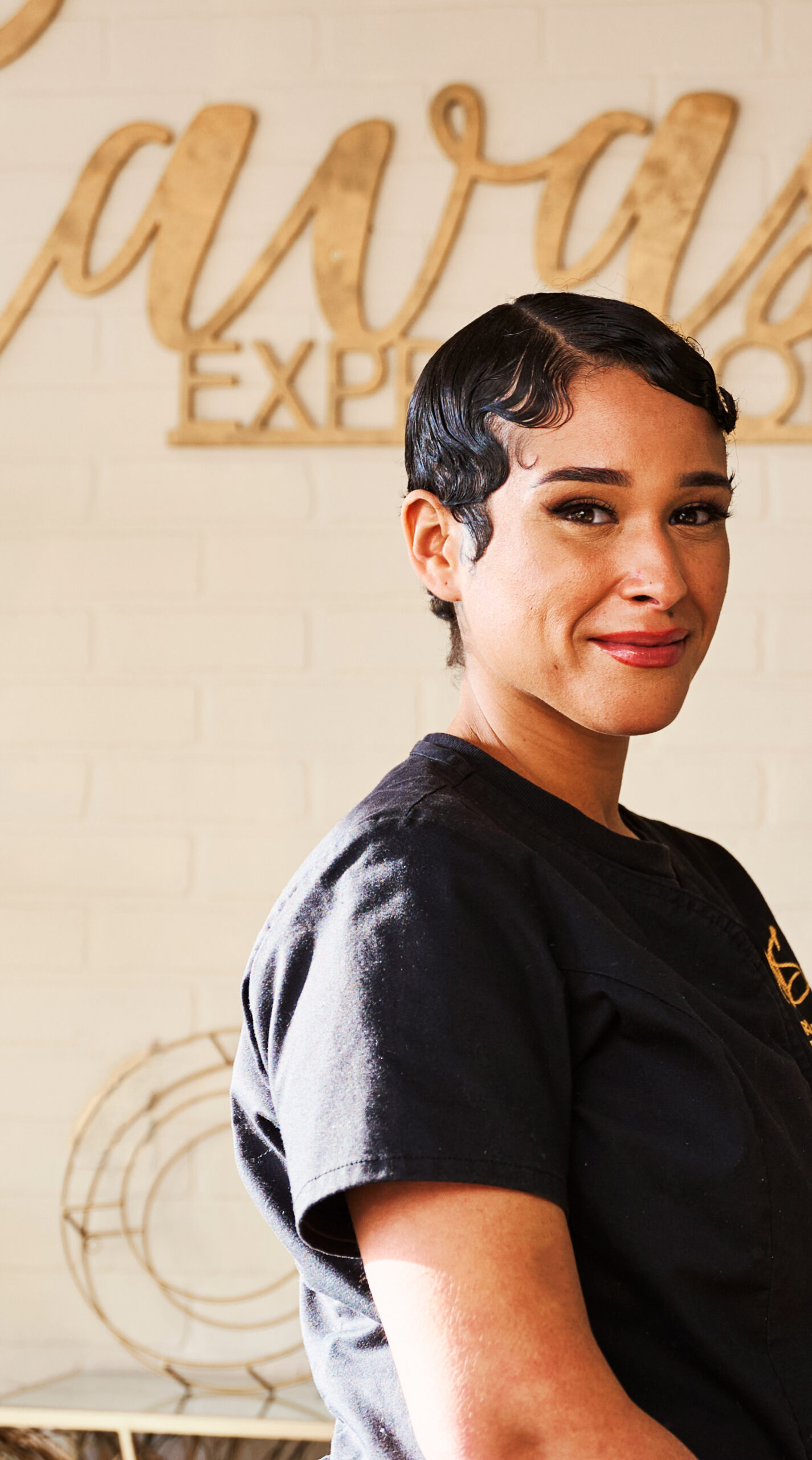 A woman with a pixie cut stares into the camera smiling without showing teeth.