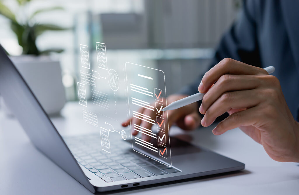 computer on a desk with a man's hands typing and holding a stylus pointing at a digital checklist while he's setting up his small business.